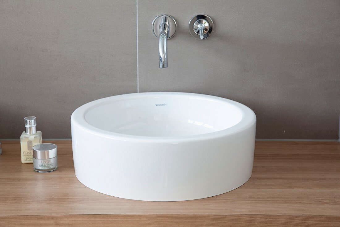 White washbasin on wooden counter and tap mounted on grey-tiled wall