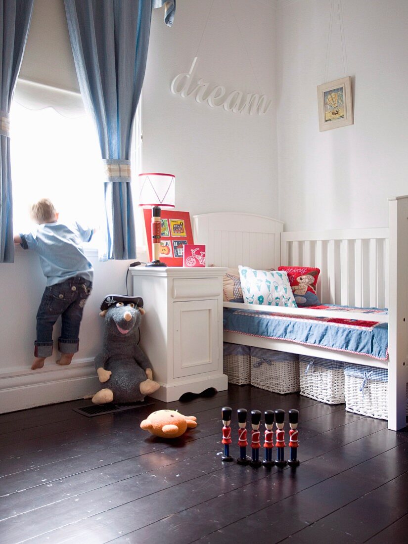 Child's bedroom in white with storage baskets below bed and wooden royal guards on dark wooden floor