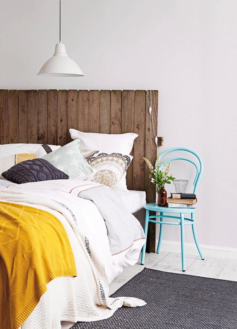 A bed with planks for a headboard and a chair for a bedside table