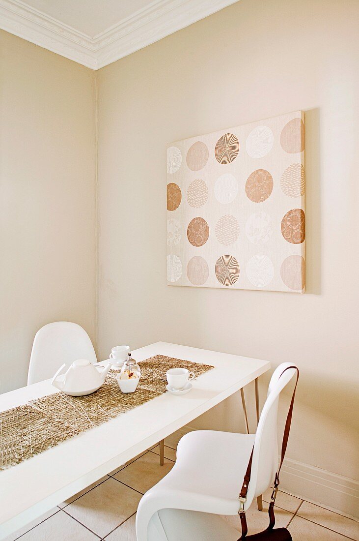 Esstisch und weiße Schalenstühle vor beige getönter Wand mit modernem Bild