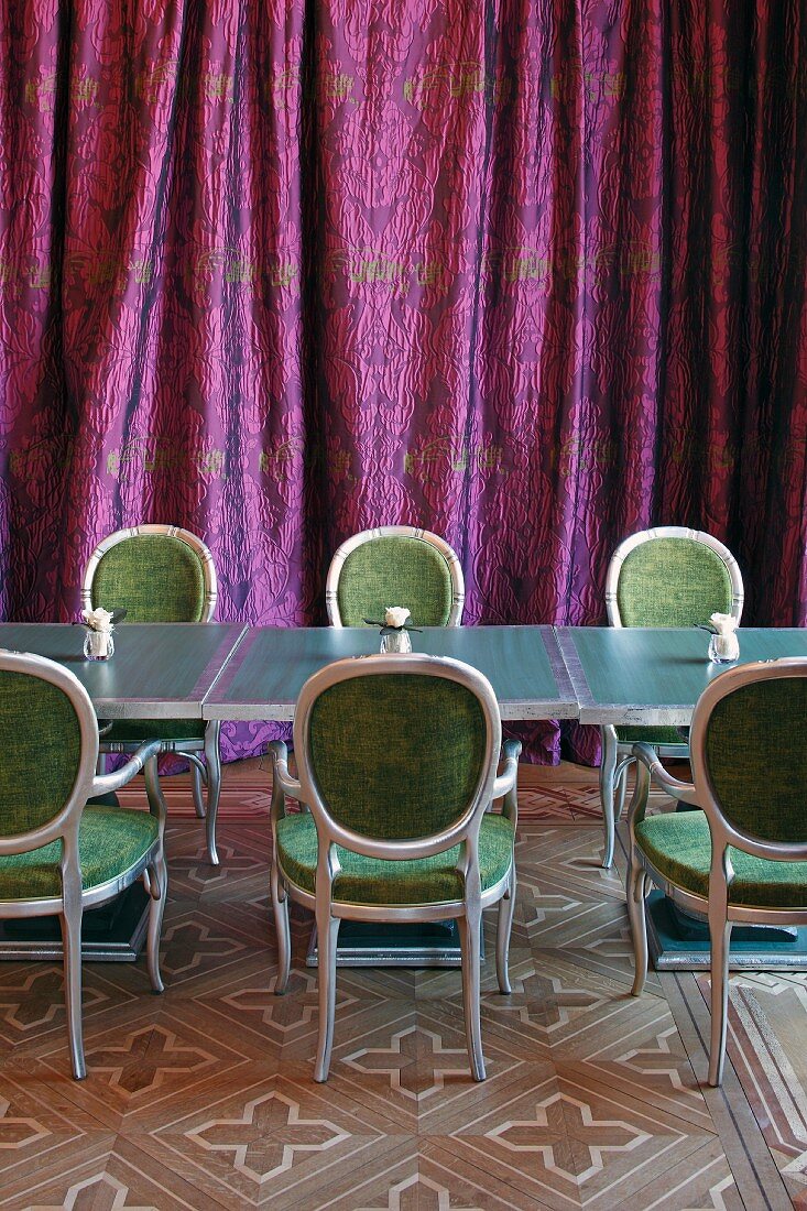 Kleine Tische mit Polsterstühlen vor violettem Vorhang im Speisesaal