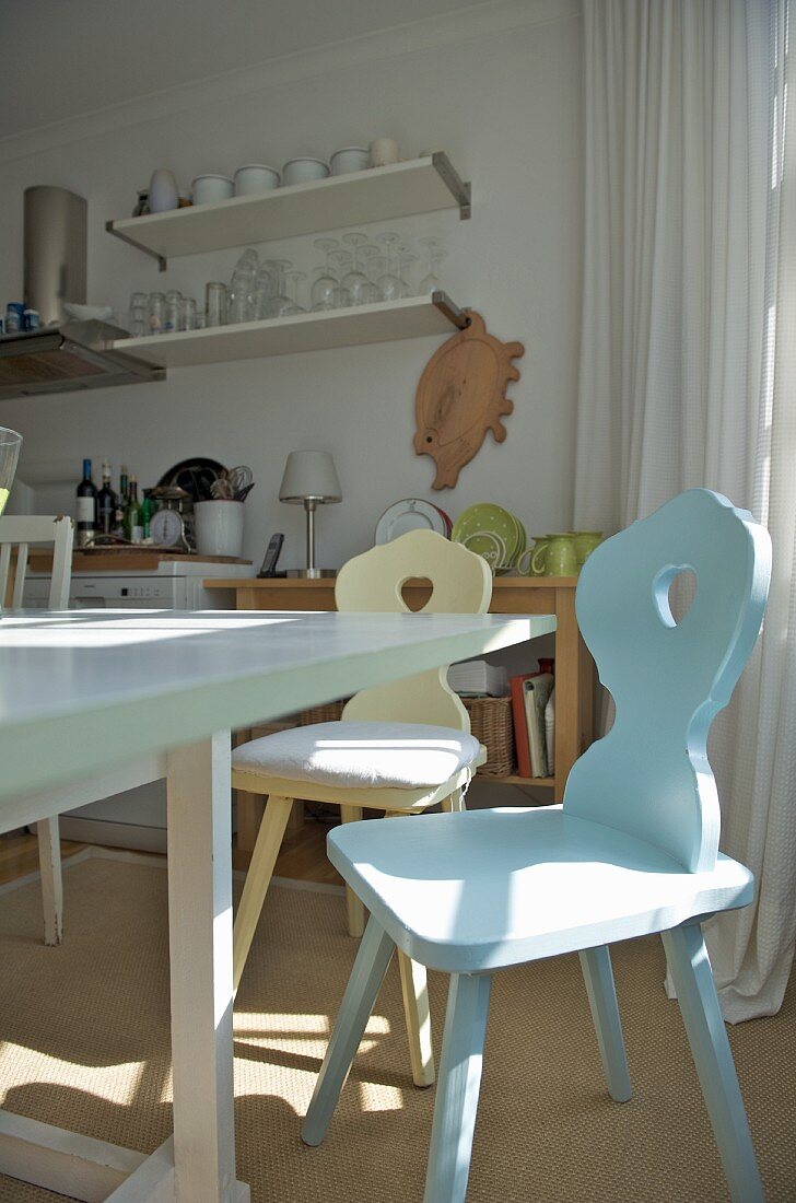 Pastellfarbene Bauernstühle an weiss lackiertem Esstisch in heller, einfacher Küche