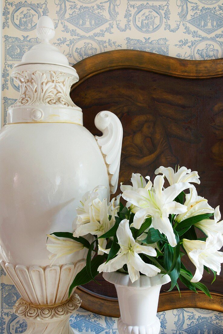 Pokalartige Vase und Blumenstrauss vor Bild an tapezierter Wand mit weiss blauen Motiven