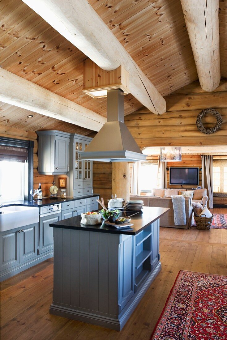 Landhausküche mit Mittelblock und hellgrau lackierten Holzfronten in offenem Wohnraum eines Blockhauses