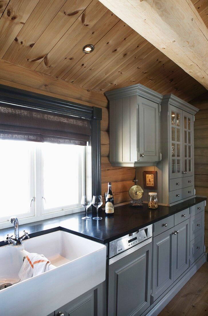 Hellgrau lackierte Holzfront an Unterschränken und Hängeschränken einer Landhausküche im Holzhaus