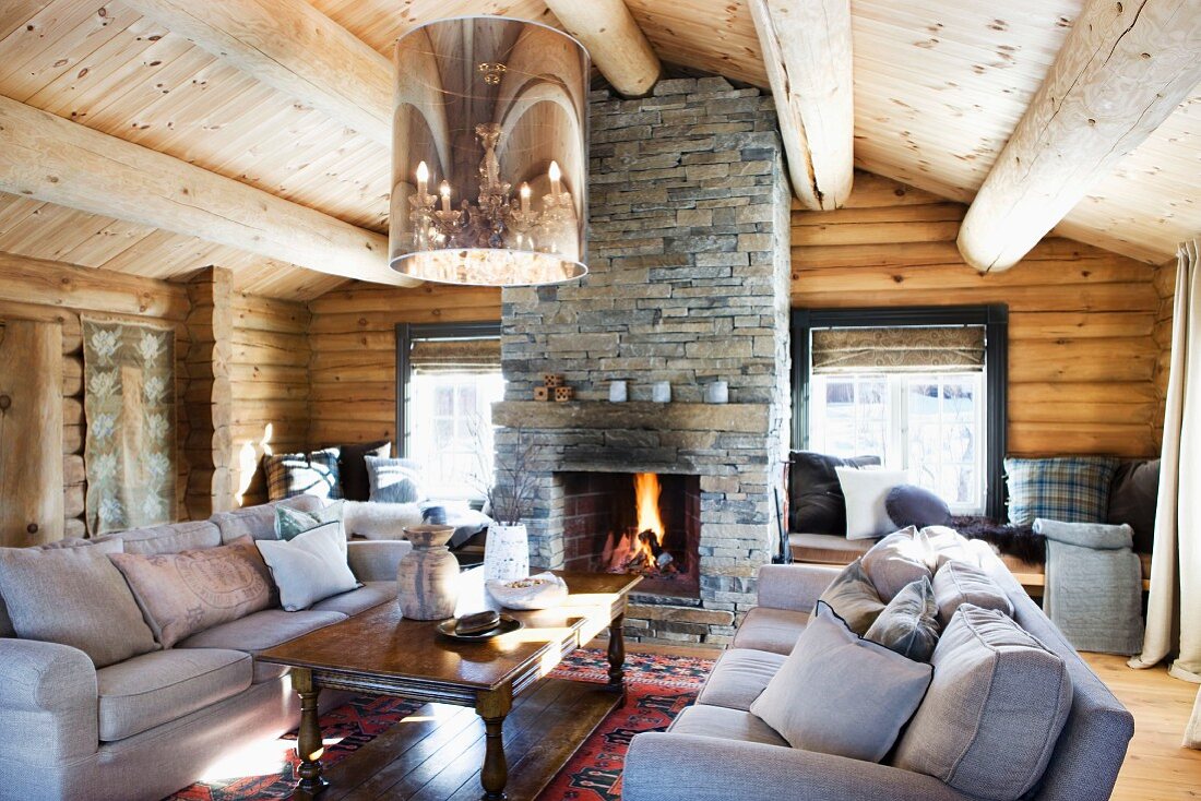 Gemütliche Sofagarnitur und Holz Couchtisch unter moderner Deckenleuchte mit Retro Touch im Wohnraum einer Blockhütte mit offenem Kamin