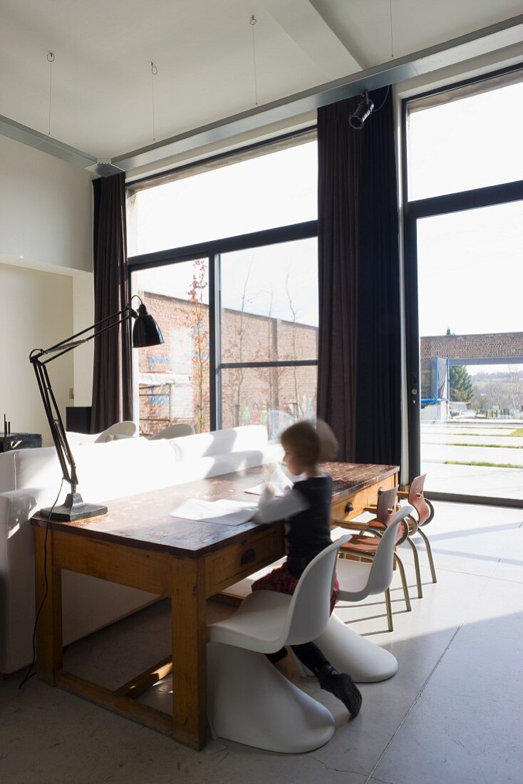 Wohnzimmer mit durchgehender Fensterfassade in einem umgenutztem Schulhaus - Panton Chairs kombiniert mit alter Schulbank und Stühlen