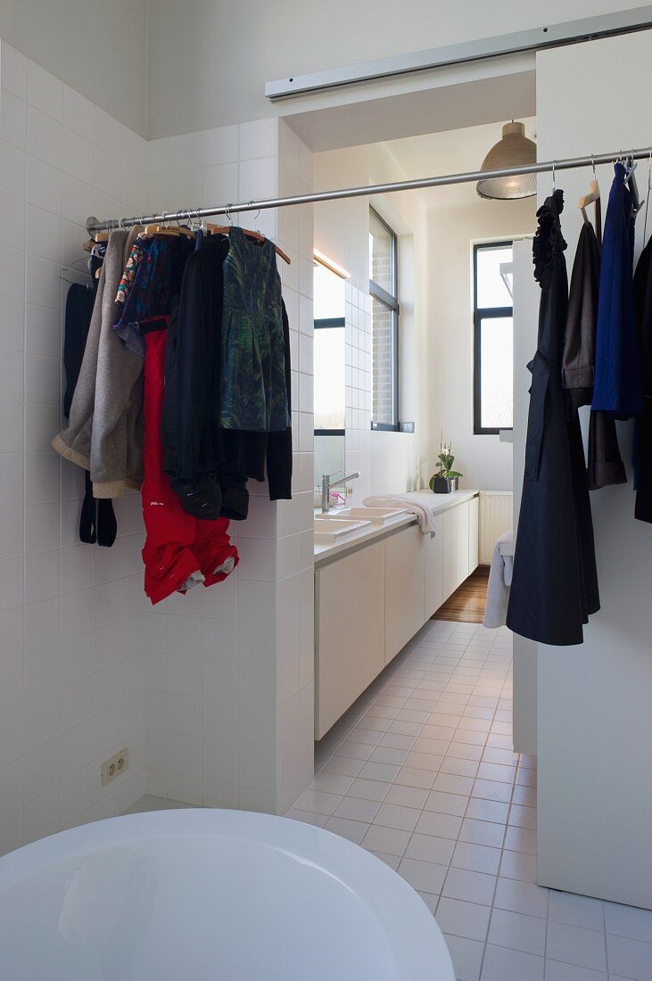 Verschiedene Kleidung an einer Stange und Blick auf langen Waschtisch im angrenzenden Raum