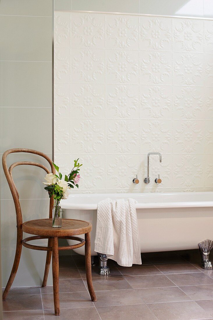 Thonet chair next to bathtub with vintage-style feet against tiled wall