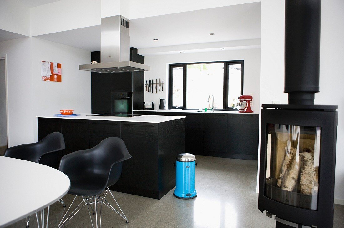 Modern interior in black and white - dining area with classic chairs in front of free-standing kitchen island and log burner