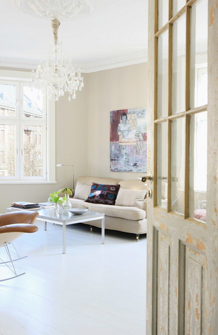 Blick durch offene Tür ins Wohnzimmer mit modernem Couchtisch und Sofa unter Kronleuchter