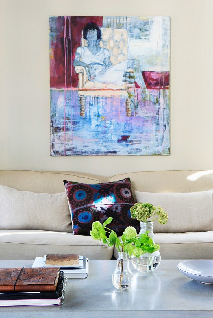 Blumen auf Couchtisch vor modernem Sofa und Gemälde an hellgrauer Wand