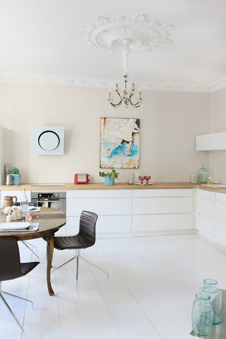 Anitker Esstisch und moderne Stühle in renovierter Küche mit Stuckarbeiten an Wand und Decke