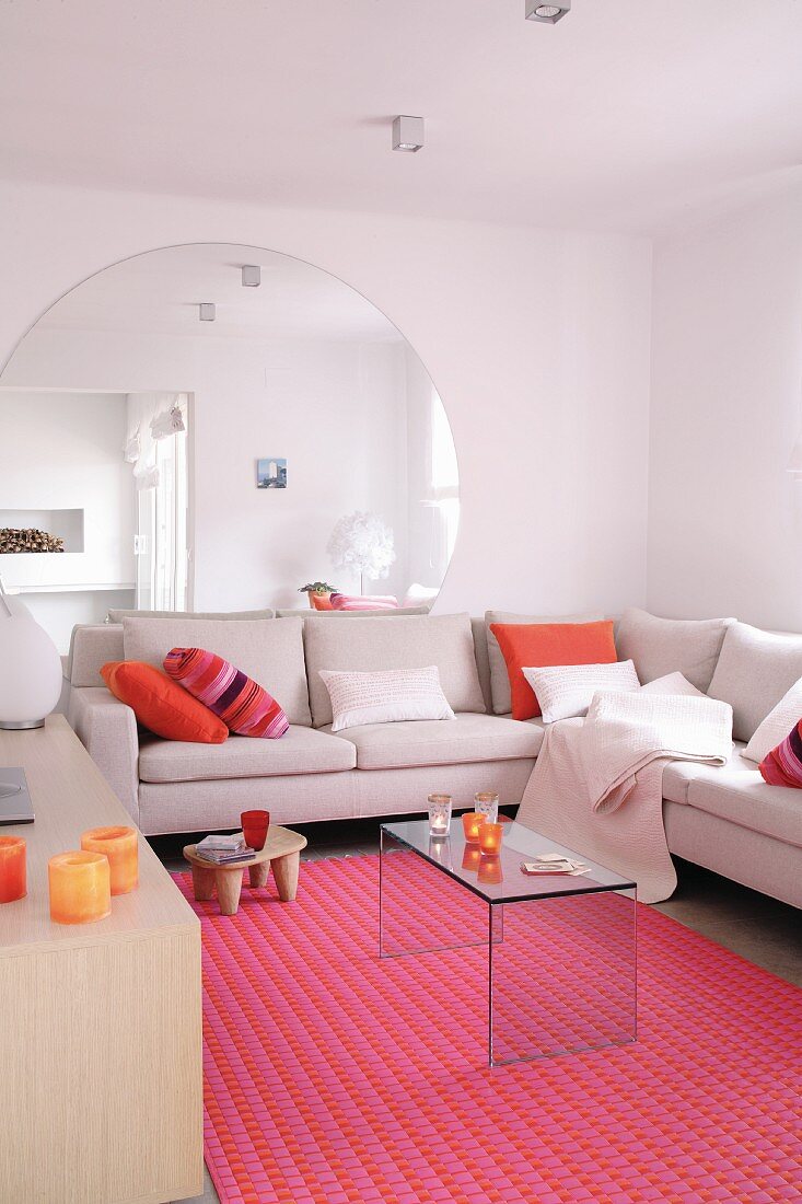 Grosser, runder Wandspiegel hinter Überecksofa mit Plexiglastisch und pinkfarbenem Teppich