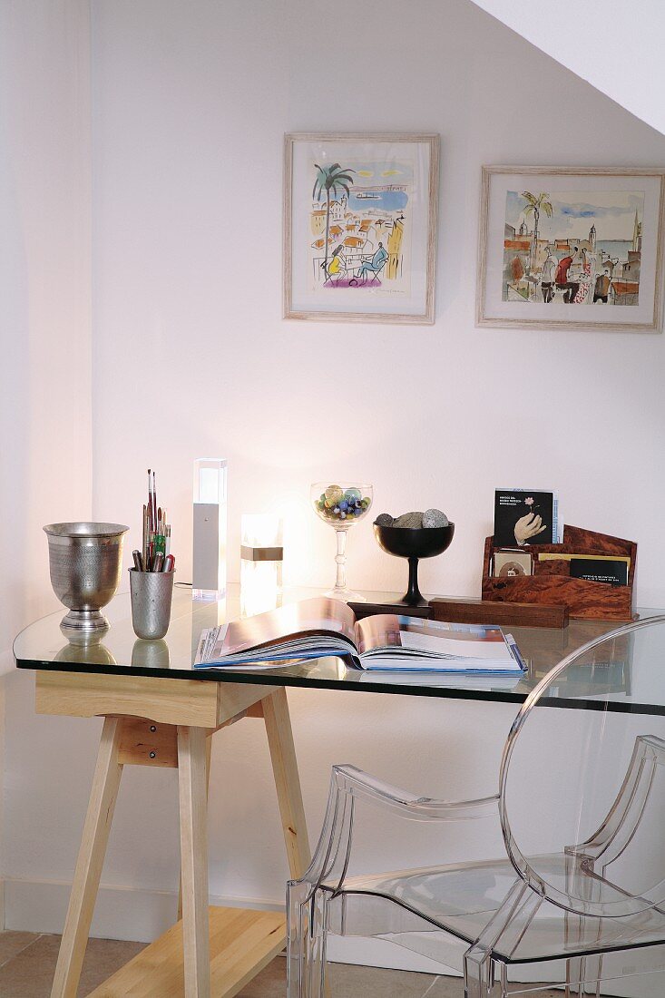 Writing area in mixture of styles with desk made from glass top and wooden trestle and designer plexiglass chair