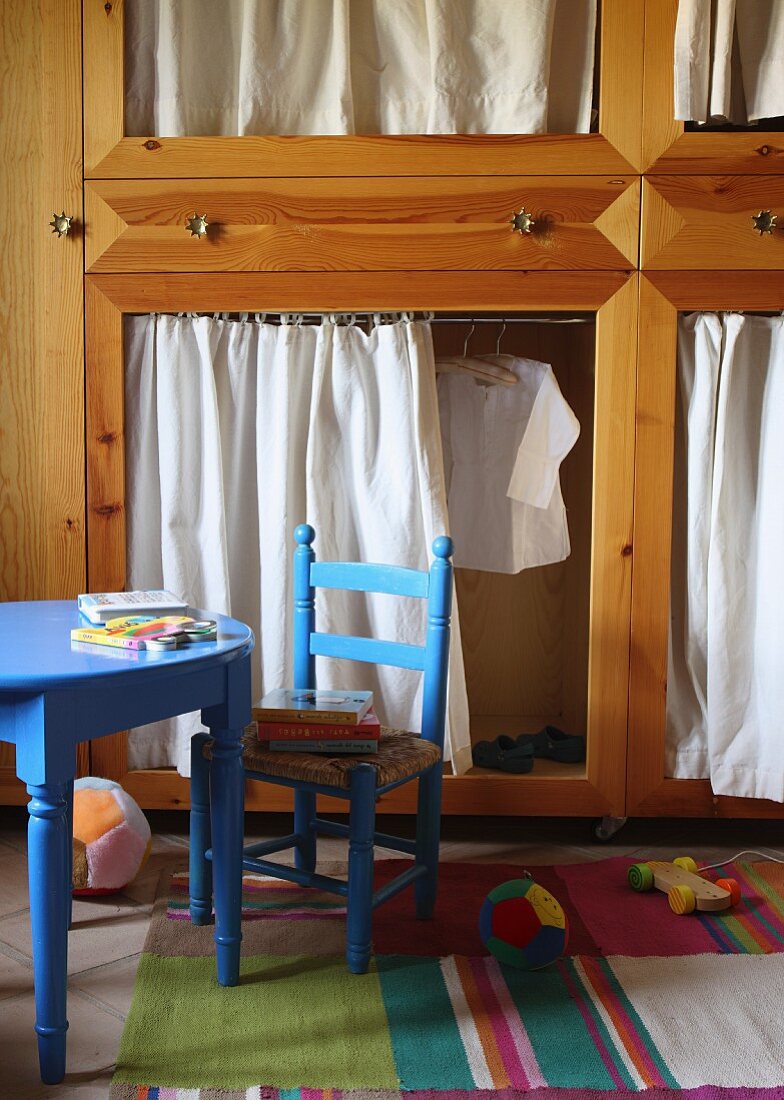 Blue child's chair and blue table in front of wooden cupboard with curtains for doors