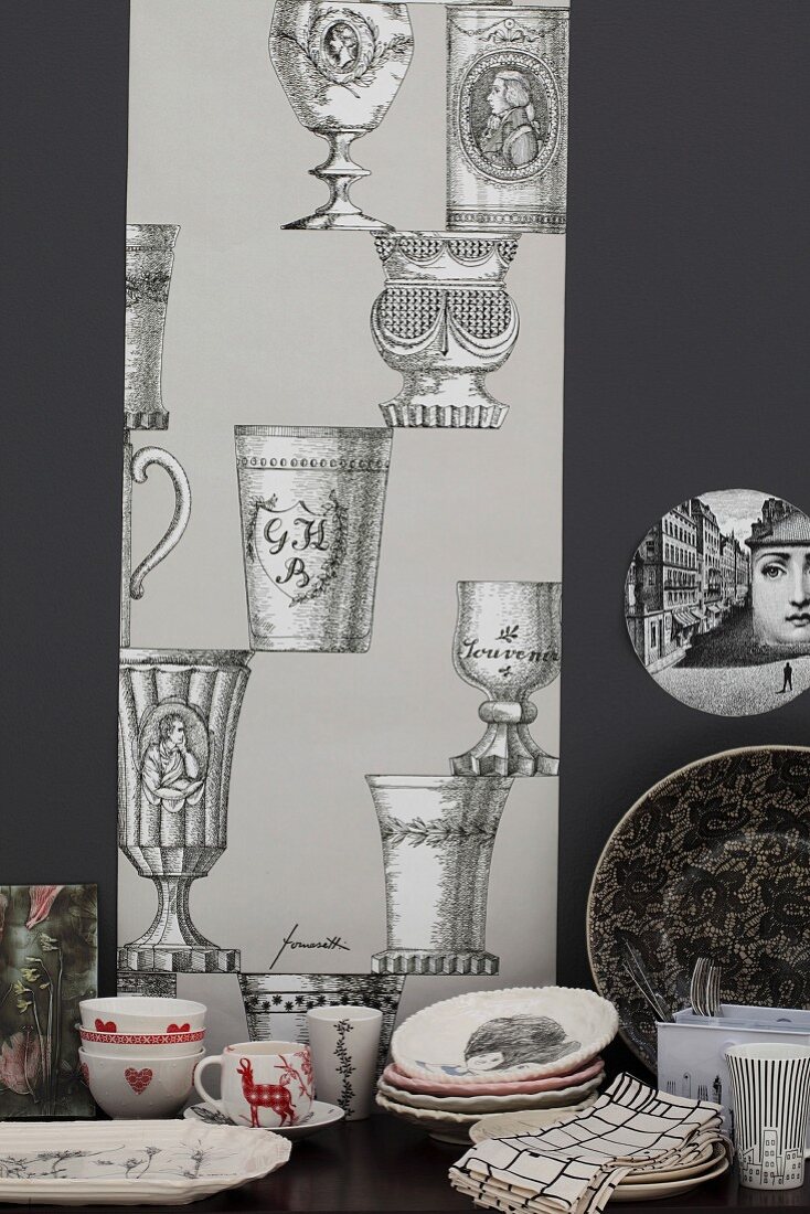 Geschirr auf Tisch vor läuferartigem Streifen an schwarzer Wand mit Pokalmotiven