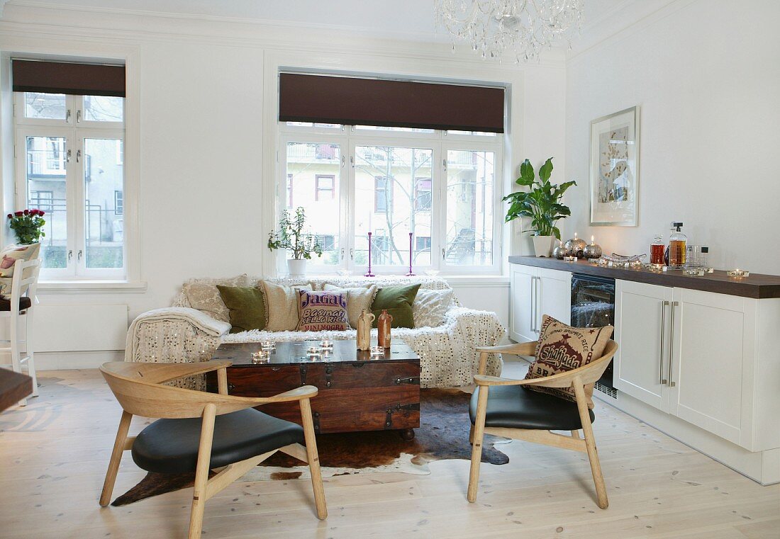 Wooden chairs and trunk-like coffee table next to white sideboard in open-plan interior