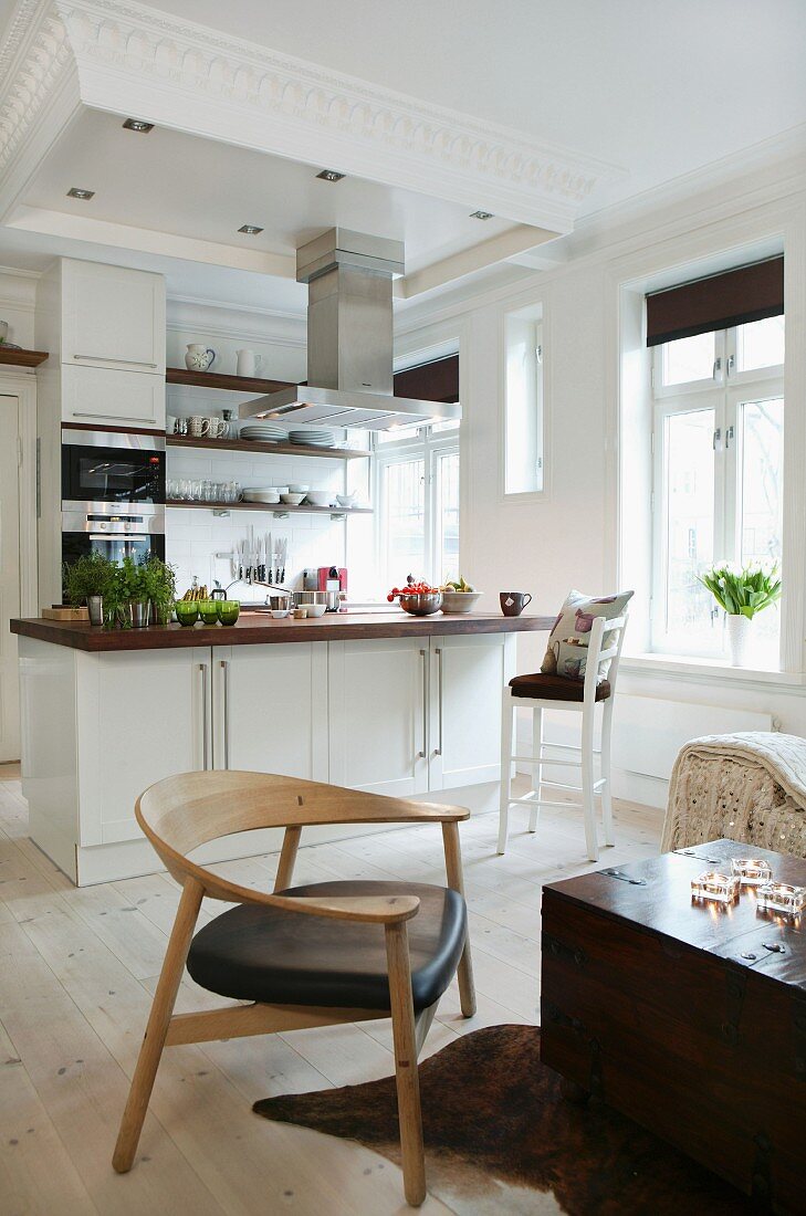 Moderner Holzstuhl vor kastenartigem Couchtisch und offene Küche mit Mittelblock im Wohnraum