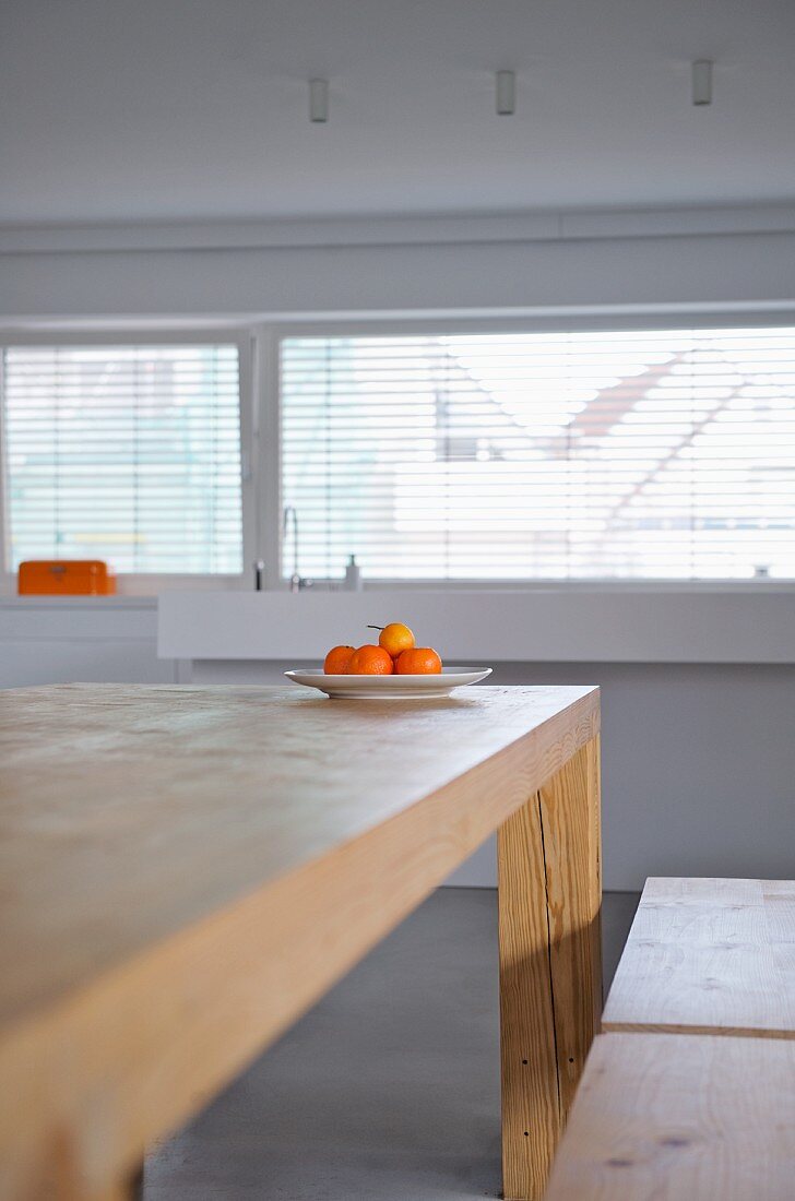Plate of tangerines on minimalist wooden table in modern interior with half-closed blinds at windows