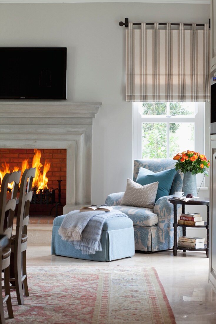Upholstered armchair and footstool next to blazing open fire