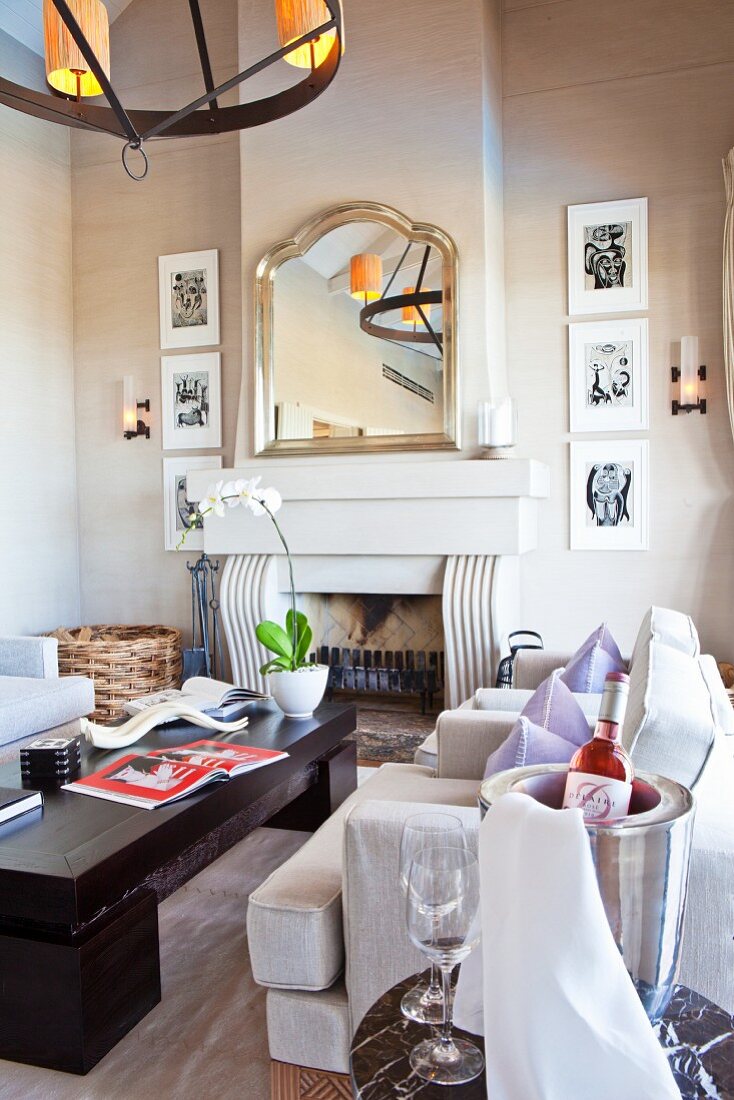 weiße Polstersessel und Holz Couchtisch vor offenem Kamin unter Spiegel mit Silberrahmen an Wand in elegantem Ambiente