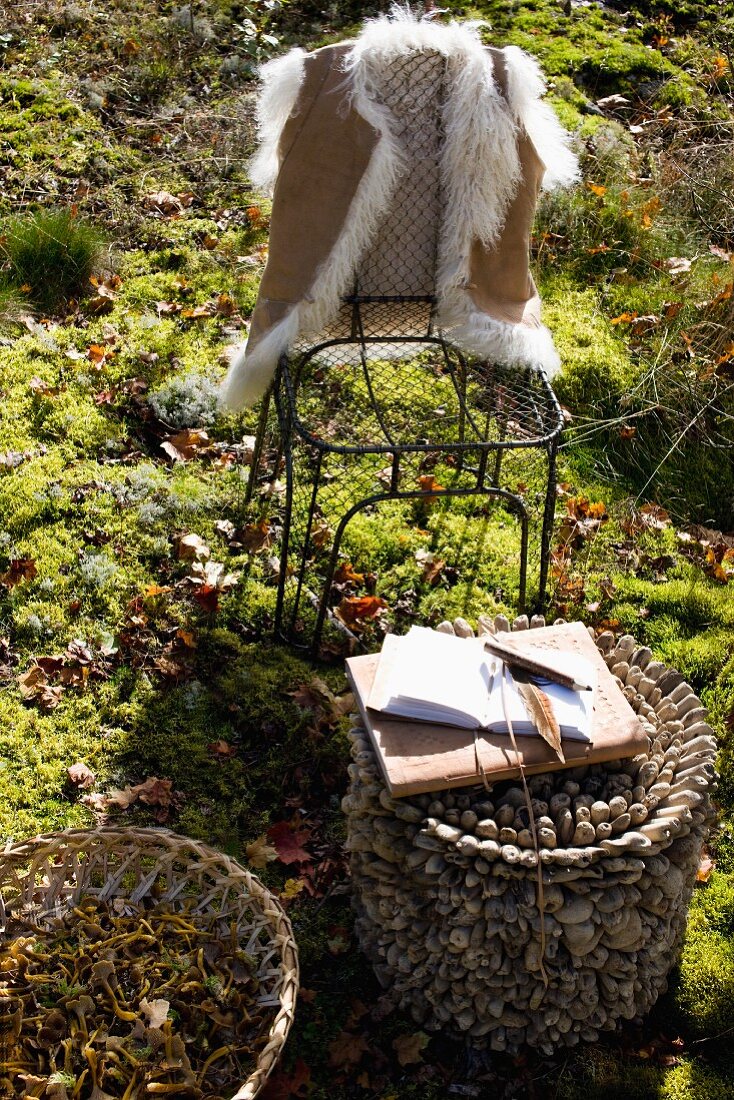 Fur waistcoat hanging on wire chair behind open notebook and pen on small, artistic side table in sunny woodland clearing