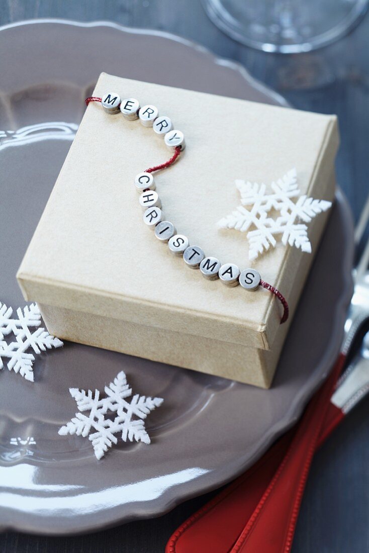 Festive gift box with string of lettered beads reading 'Merry Christmas' and stylised snowflakes