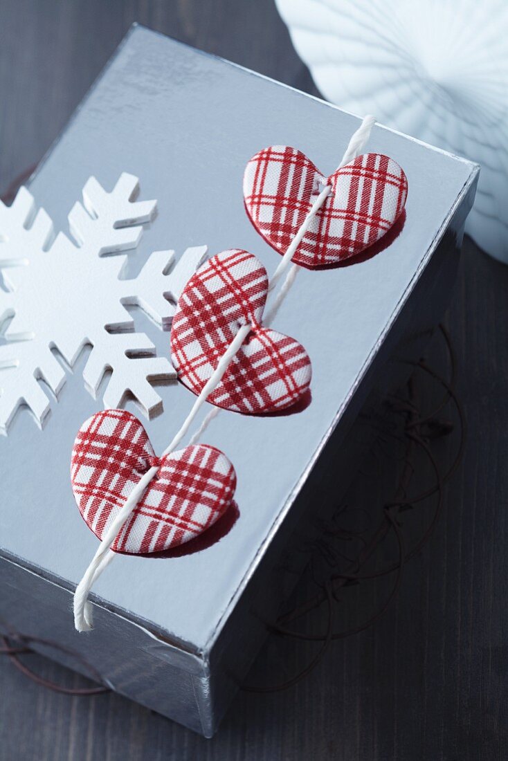 Wrapped Christmas present decorated with red and white checked fabric hearts and wooden snowflake