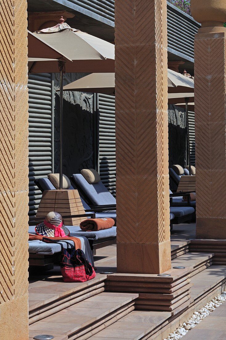 Sonnenliegen und Schirme hinter Mauerstützen auf der Terrasse eines Hotels im Art Déco Stil