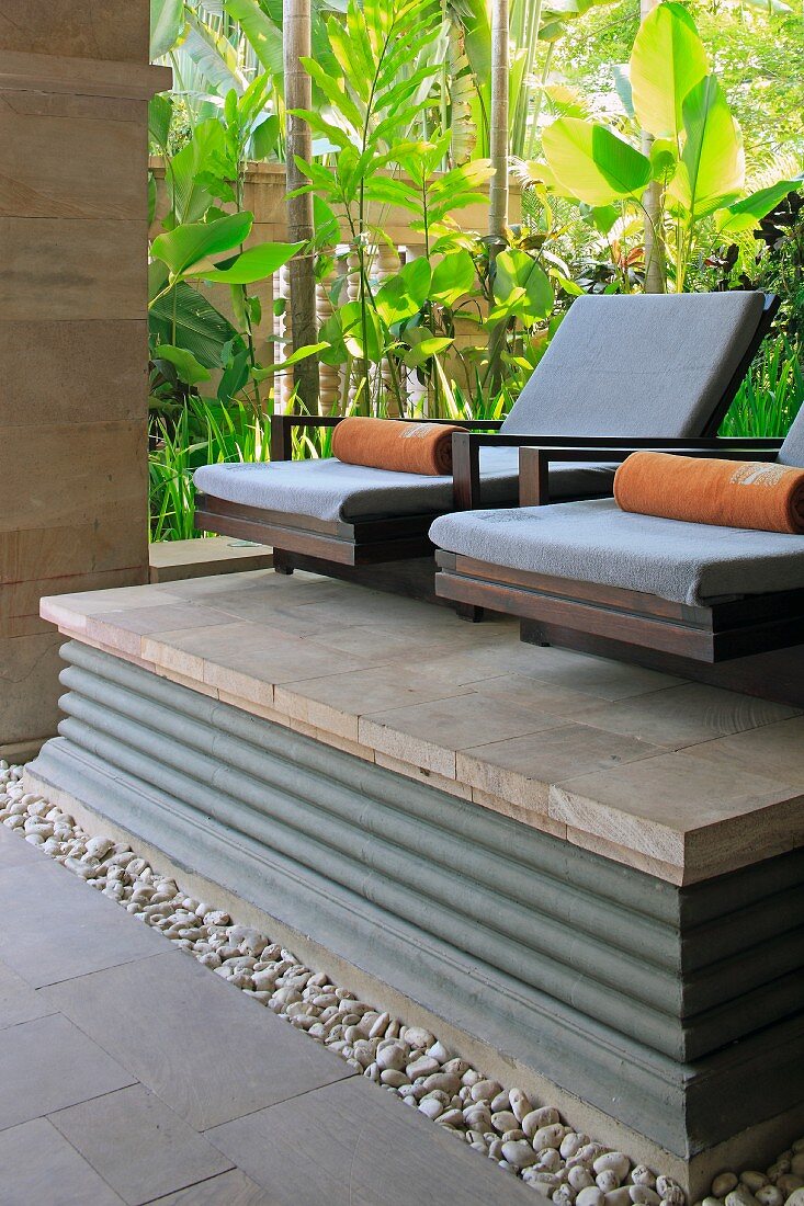 Spa armchairs on stone platform in front of tropical foliage plants