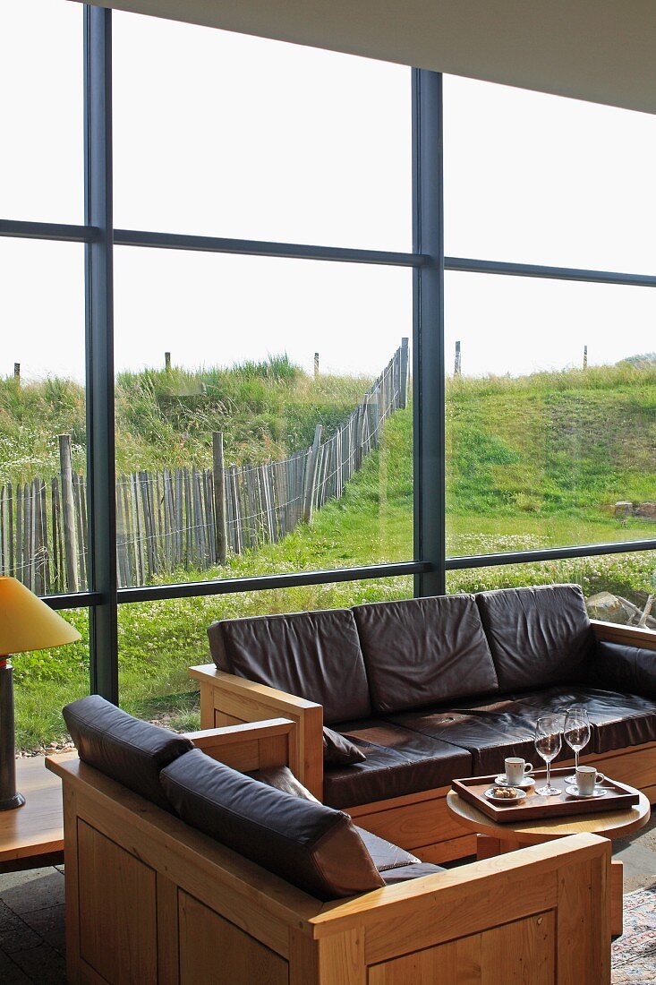 Sitzgarnitur aus kubischen Holzelementen mit Lederpolstern; Fensterfront mit Blick auf Wiesenlandschaft