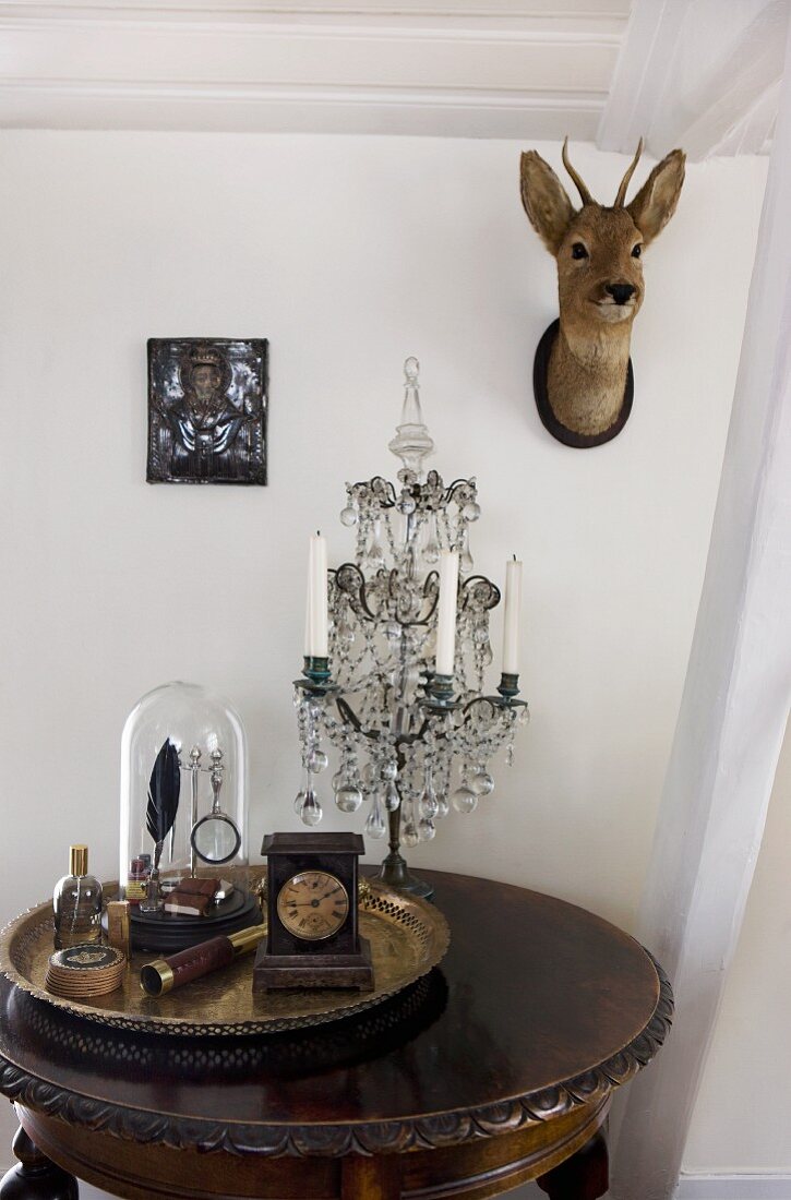 Messingtablett mit Sammlung antiker Gegenstände und Kerzenhalter auf Beistelltisch; Rehkopf an der Wand