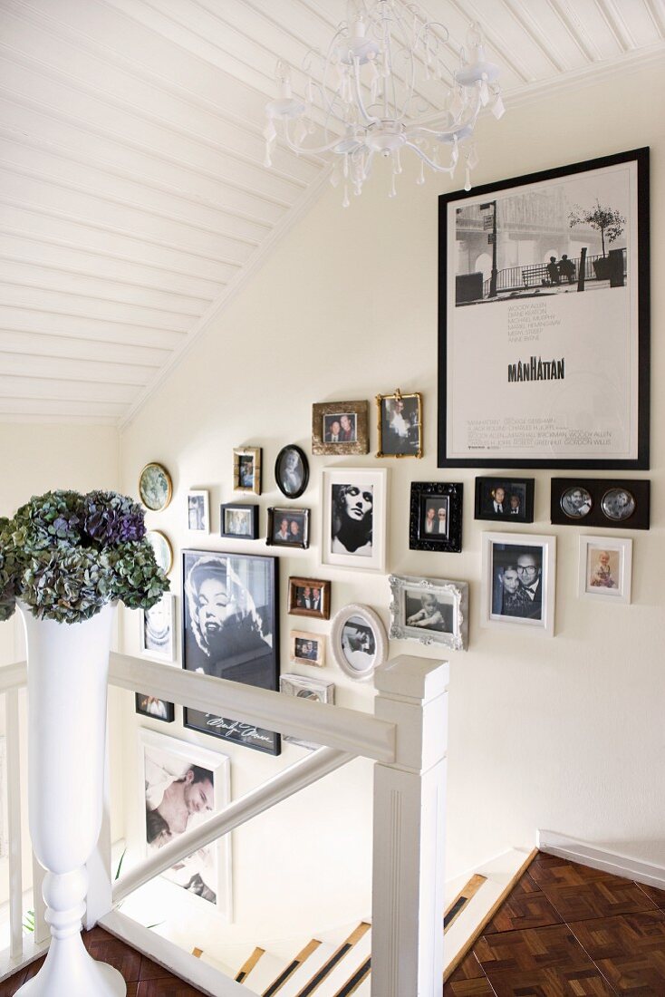 Gallery of photographs on wall of staircase with white-painted wooden elements and mosaic parquet floor