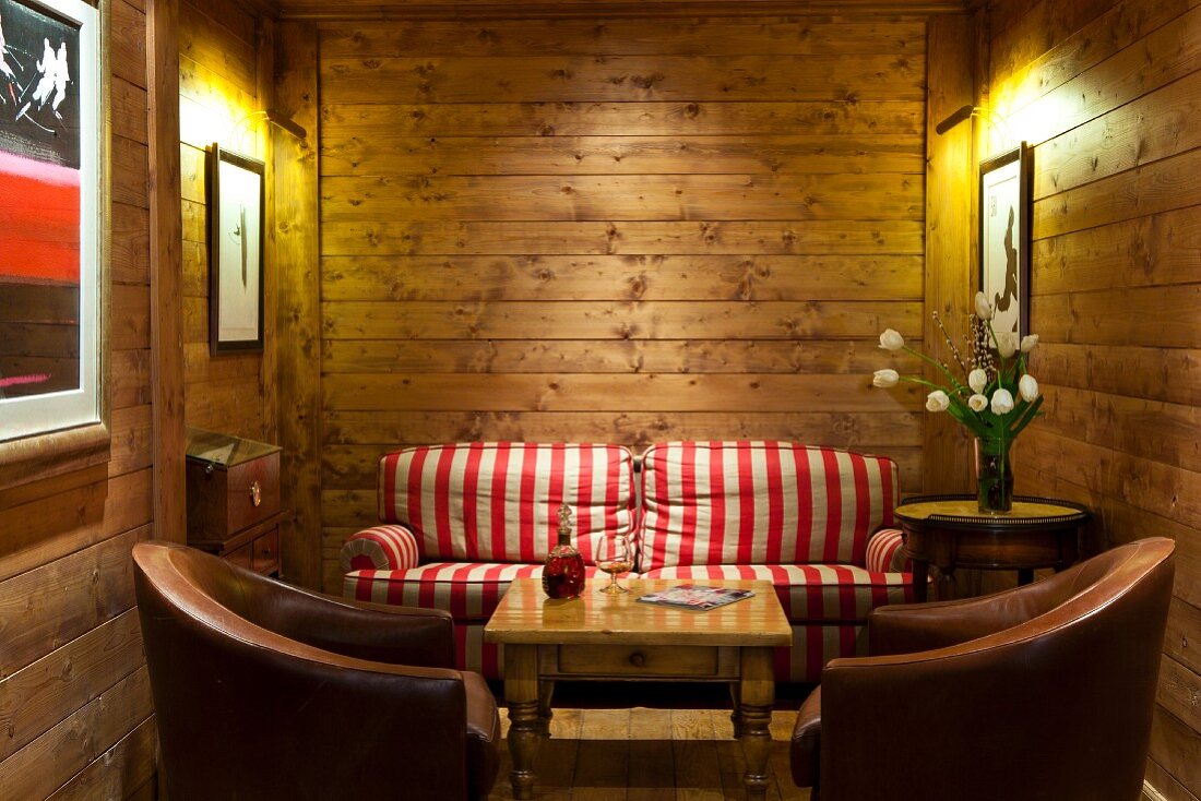 Gemütliche Sitzecke mit beleuchteten Bildern und rotweiss gestreiftem Sofa in einem Holzhaus
