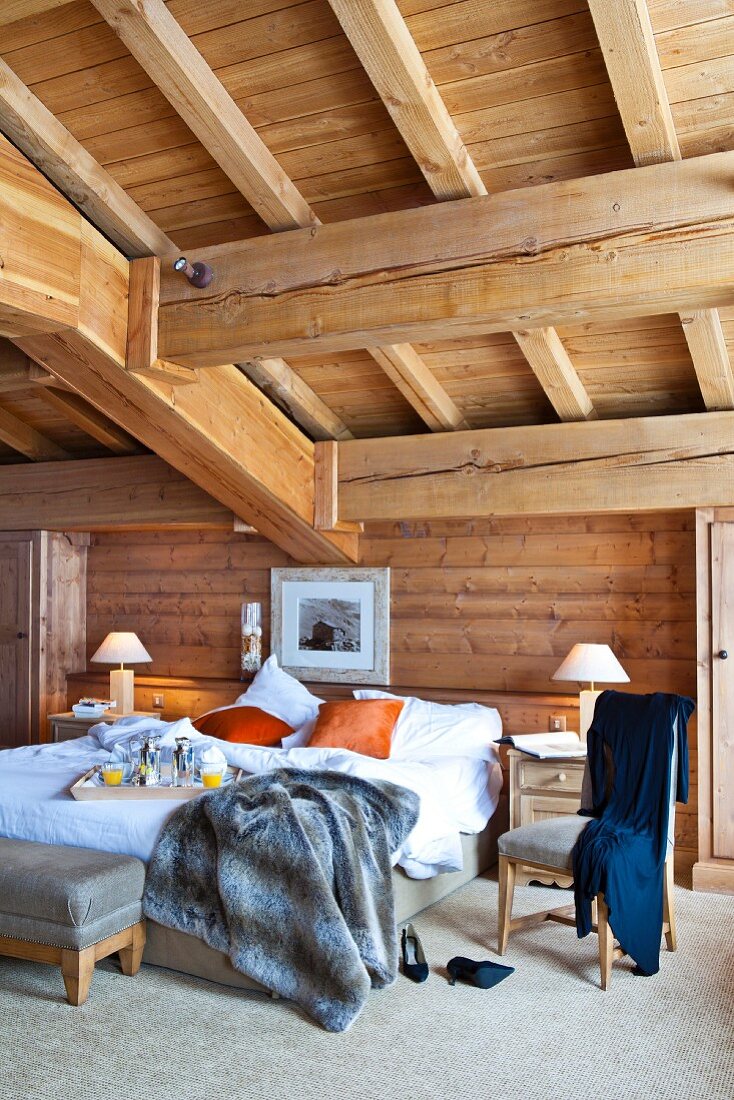 Doppelbett mit Frühstückstablett unter der massiven Holzbalkendecke eines rustikalen Schlafzimmers
