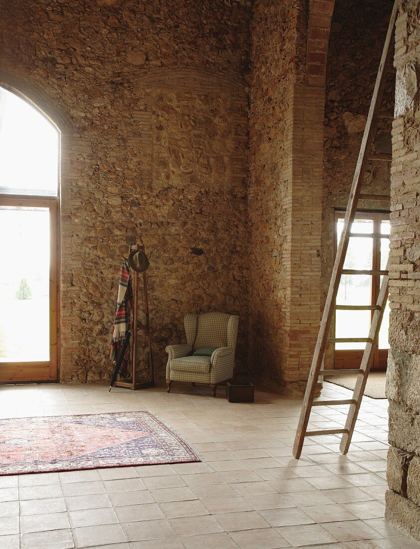 Ohrensessel und Kleiderständer in der Ecke eines hohen, restaurierten Steinhauses mediterranen Stils