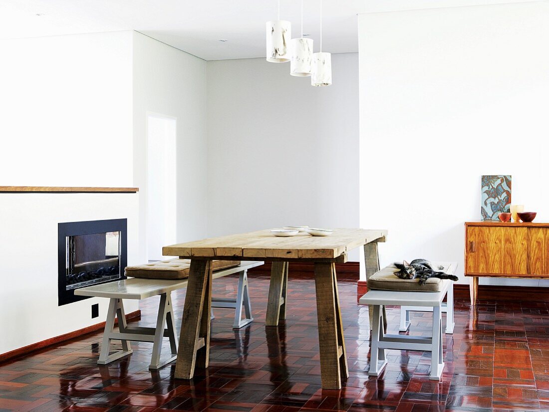 Nüchterner improvisierter Wohn- und Essbereich mit orangefarbenem glänzendem Fliesenboden, eine massive Holzplatte auf Holzböcken dient als Esstisch