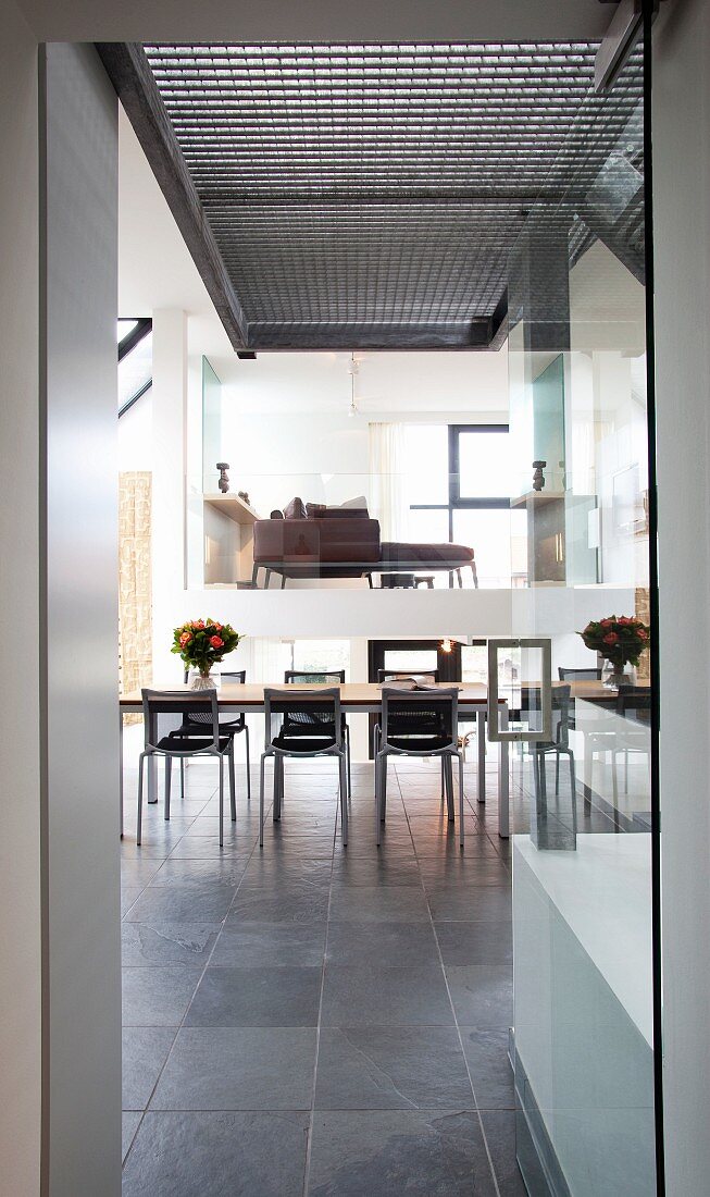 View into dining area with grey tiled floor and elevated seating area behind glass wall