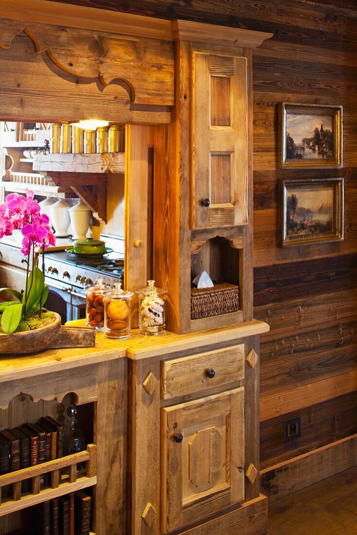 Rustic, wooden fitted cupboard with carved details and integrated serving hatch leading to kitchen