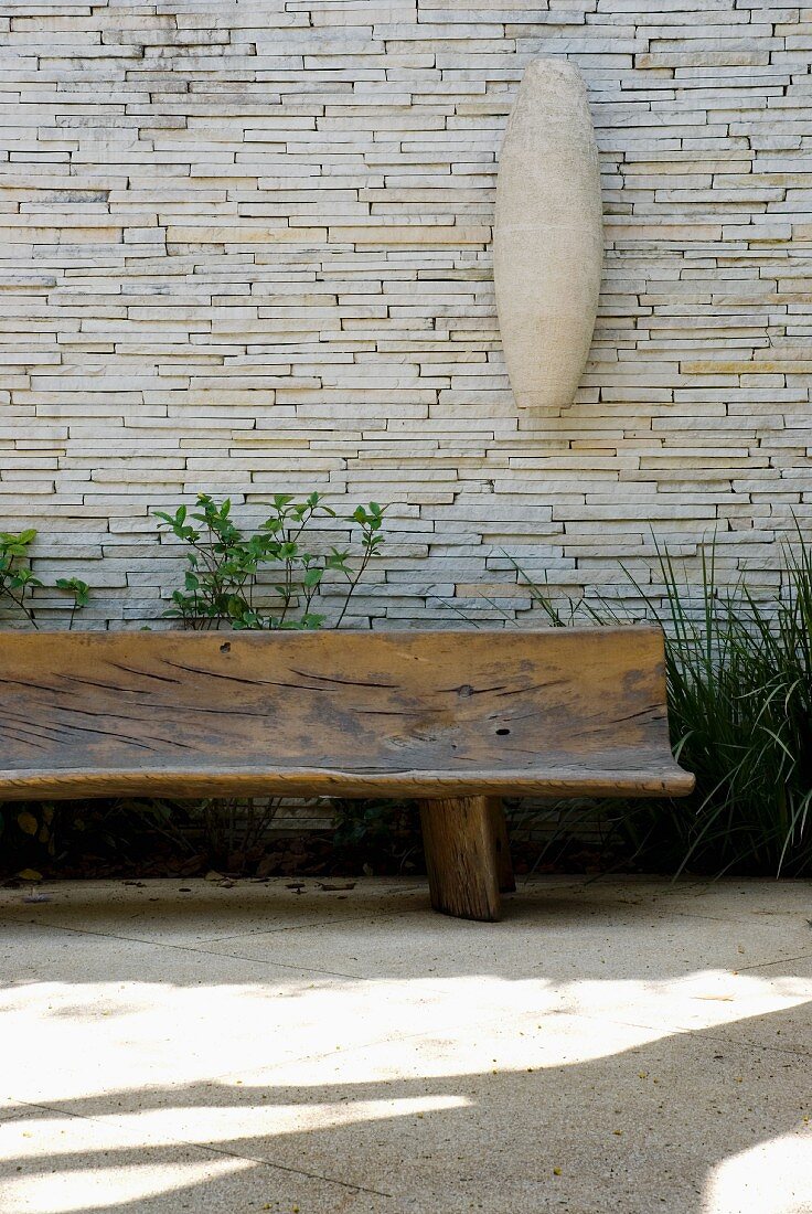 Rustic bench made from hollowed-out tree trunk against stone wall on sunny terrace