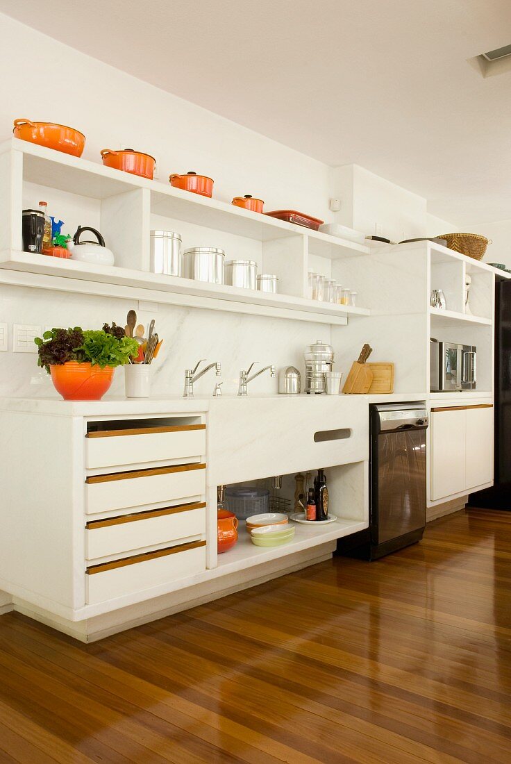 Verschiedene Töpfe in fröhlichem Orange als Farbtupfer in weisser, moderner Küche mit hochglänzendem Parkettboden