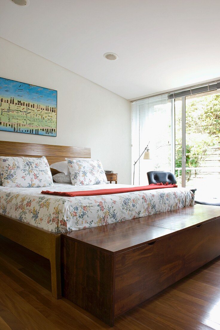 Doppelbett mit geblümtem Bezug und breite Truhe aus Edelholz in Schlafzimmer mit offener Schiebetürfront