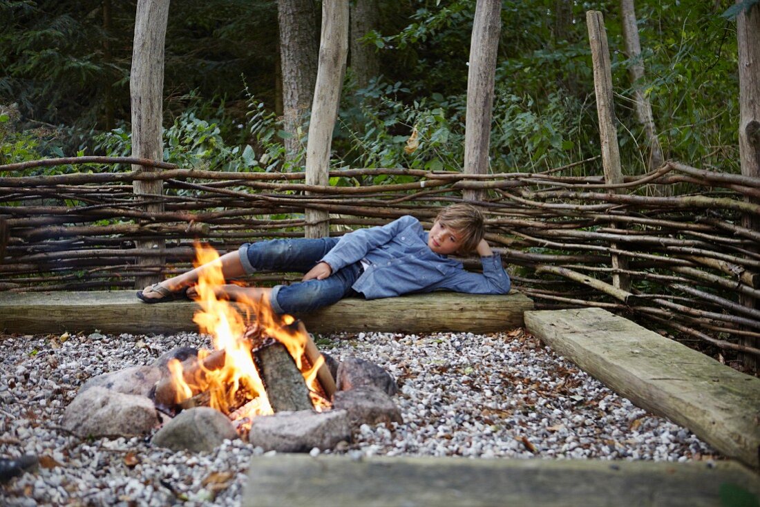 Junge liegt auf Holzstamm beim Lagerfeuer