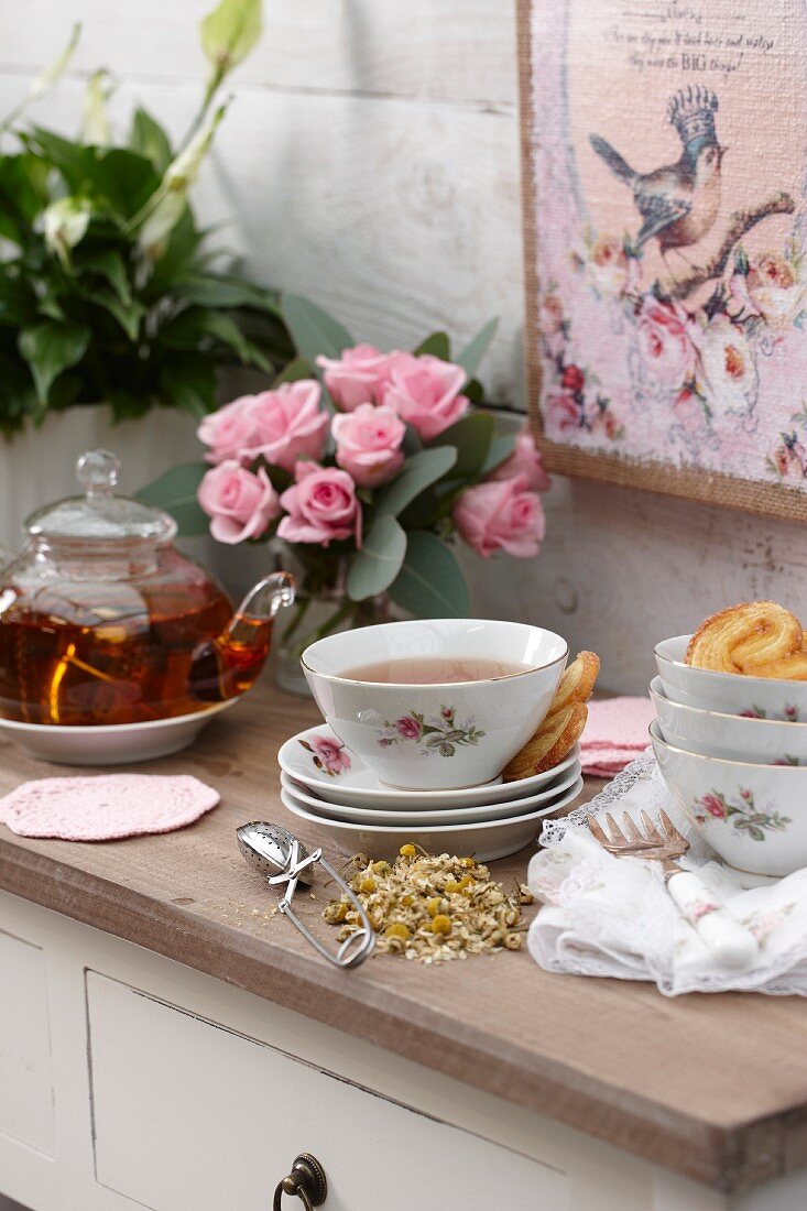 Tea, dried chamomile and pastries on cabinet