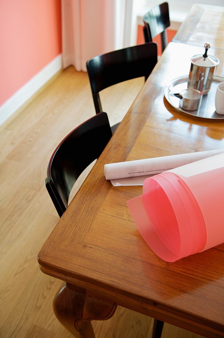 Corner of antique wooden table with roll of pink paper next to milk frother on tray
