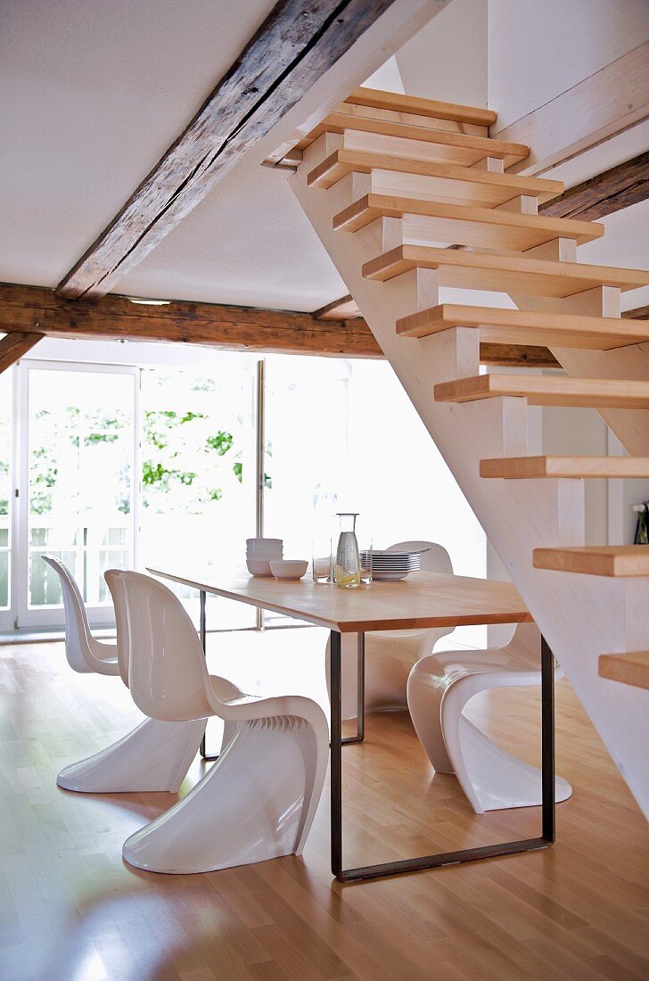 Schalenstühle aus weißem Kunststoff und moderner Esstisch in offenem Wohnraum mit Treppe
