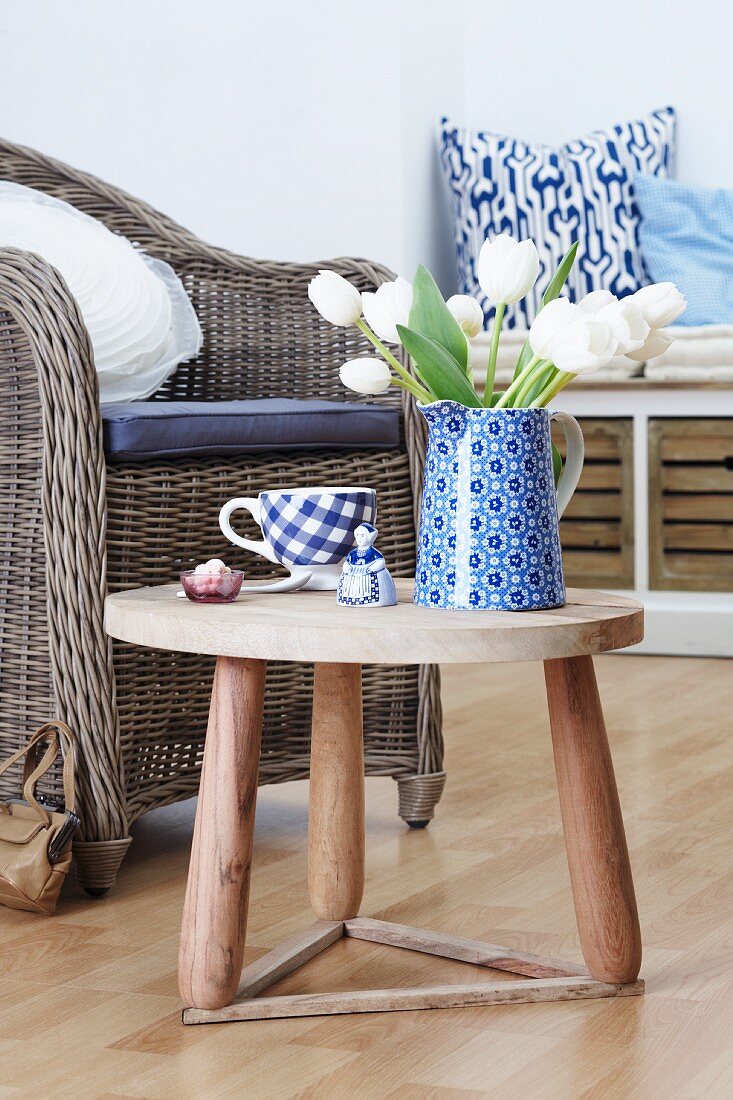 Blue jug and tulips on side table, cushions on wicker chair and scatter cushions on low storage bench