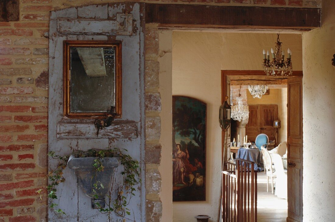 Kreative Dekoration einer alten Holztür; Blick vom rustikalen Hausflur eines französischen Landhauses in den Salon