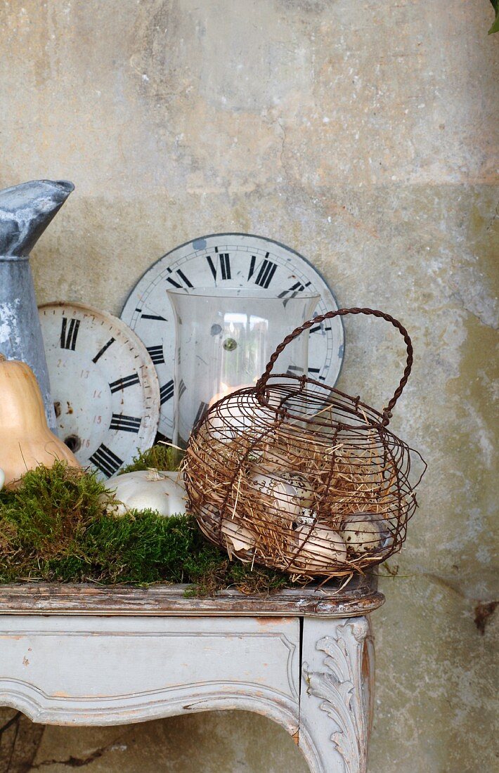 Ziffernblätter alter Uhren und Drahtkorb mit Vogeleiern auf einem Rokoko-Konsolentisch als romantische Landhausdekoration